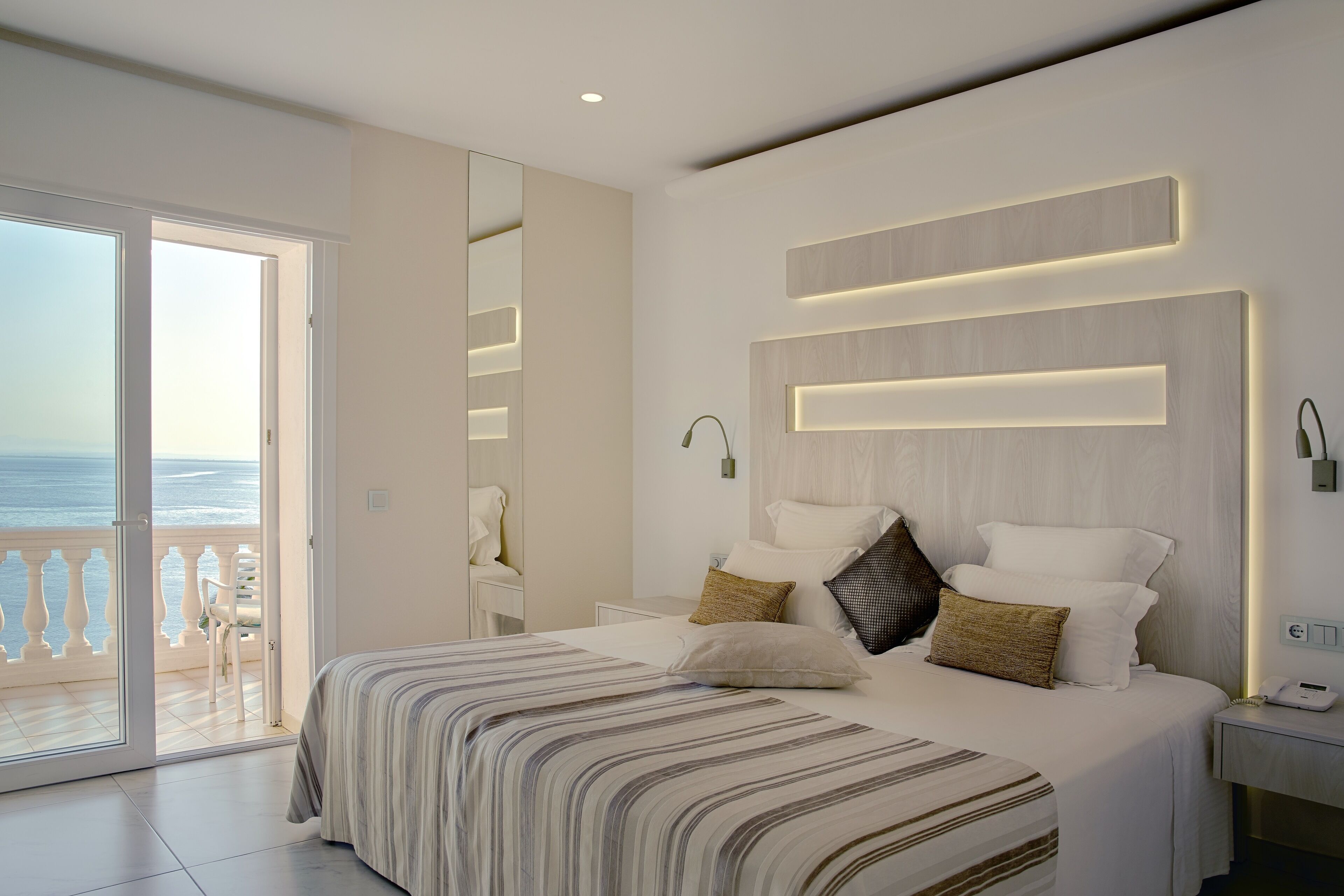 A modern bedroom with a large bed, a balcony with a view of the sea, and a minimalist design.