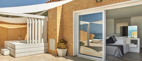 A modern hotel room with a large sliding glass door leading to a balcony with a view of the sea.