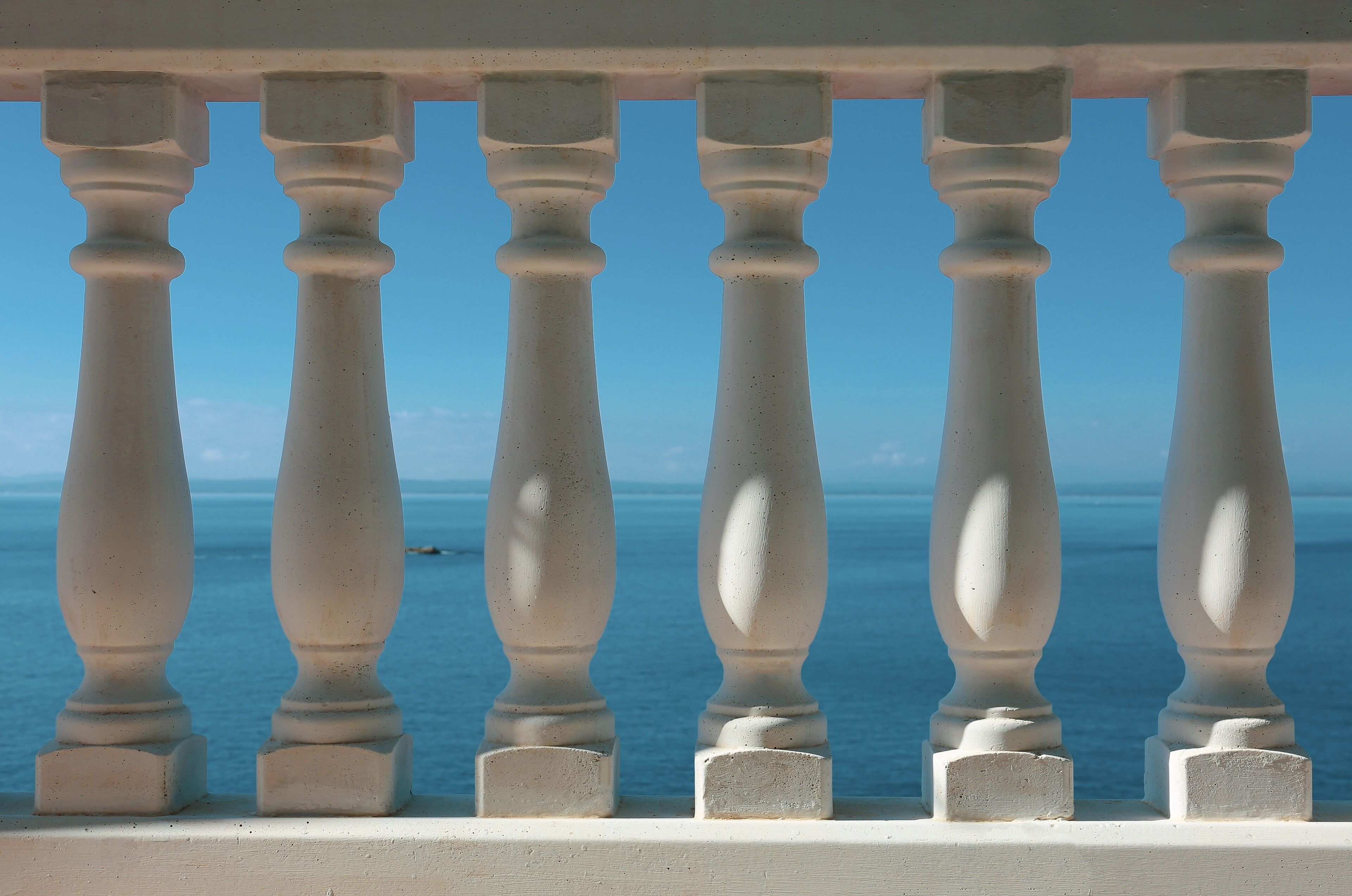 A balcony with white balustrades overlooking a clear blue sea.