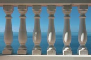 A balcony with white balustrades overlooking a clear blue sea.
