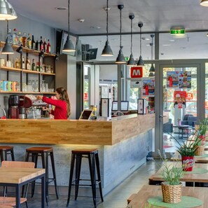 Un espace bar avec un barman, des étagères remplies de bouteilles et un coin salon avec des tables et des chaises.