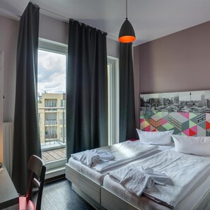 A hotel room with a bed, a chair, a window with curtains, and a cityscape view. - Meininger Hotel Berlin Prenzlauer Berg (Berlin)