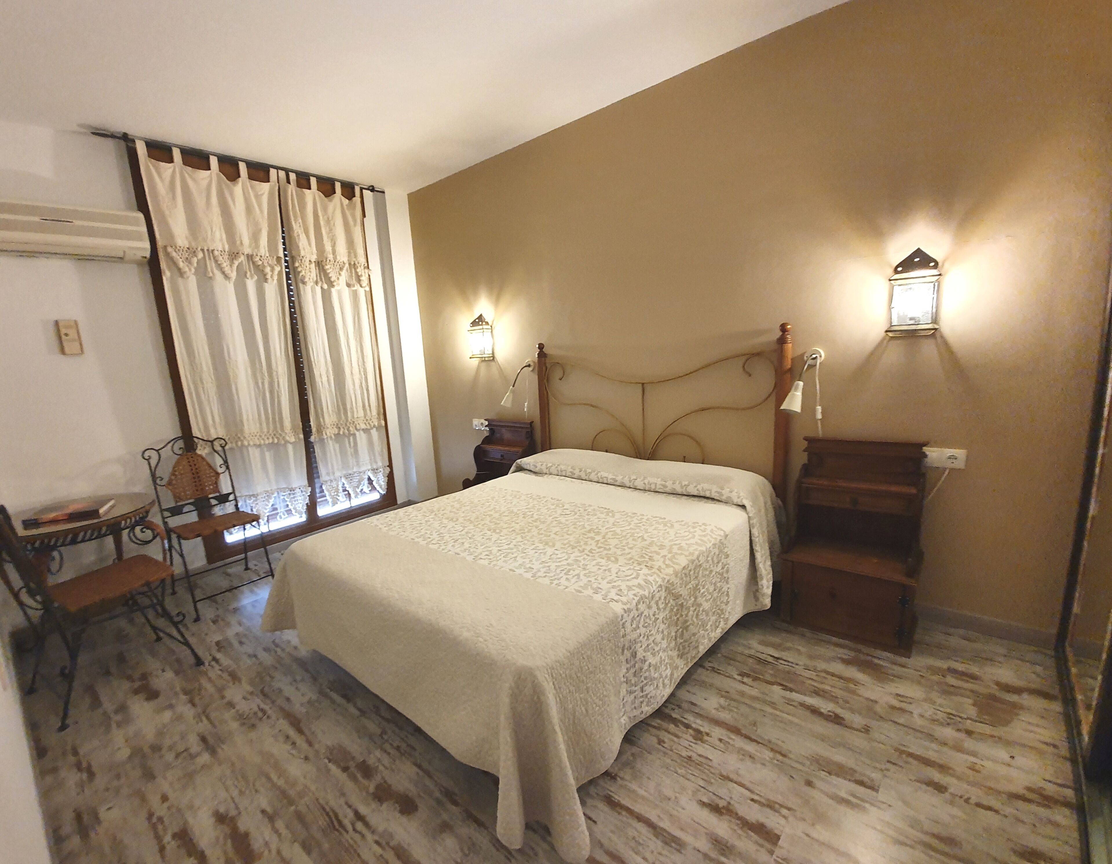 Une chambre à coucher avec un lit, une table de chevet, une lampe, une chaise, une table et des rideaux.