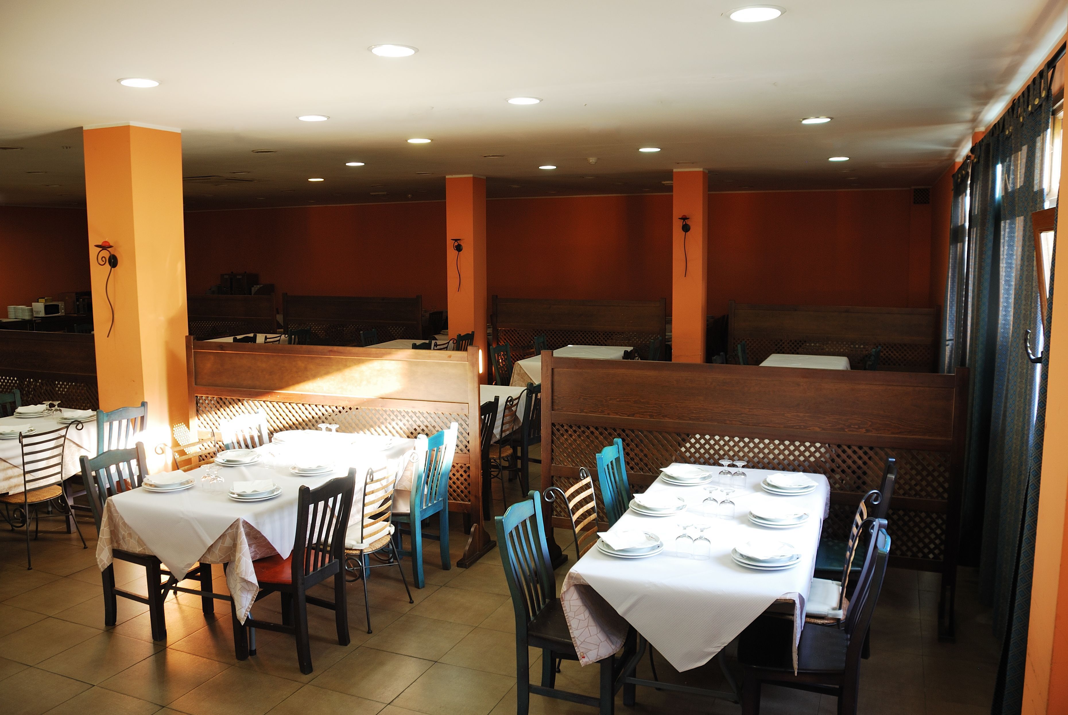 Un restaurant doté de nombreuses tables et de banquettes, chacune étant agrémentée d’une nappe blanche et d’assiettes.