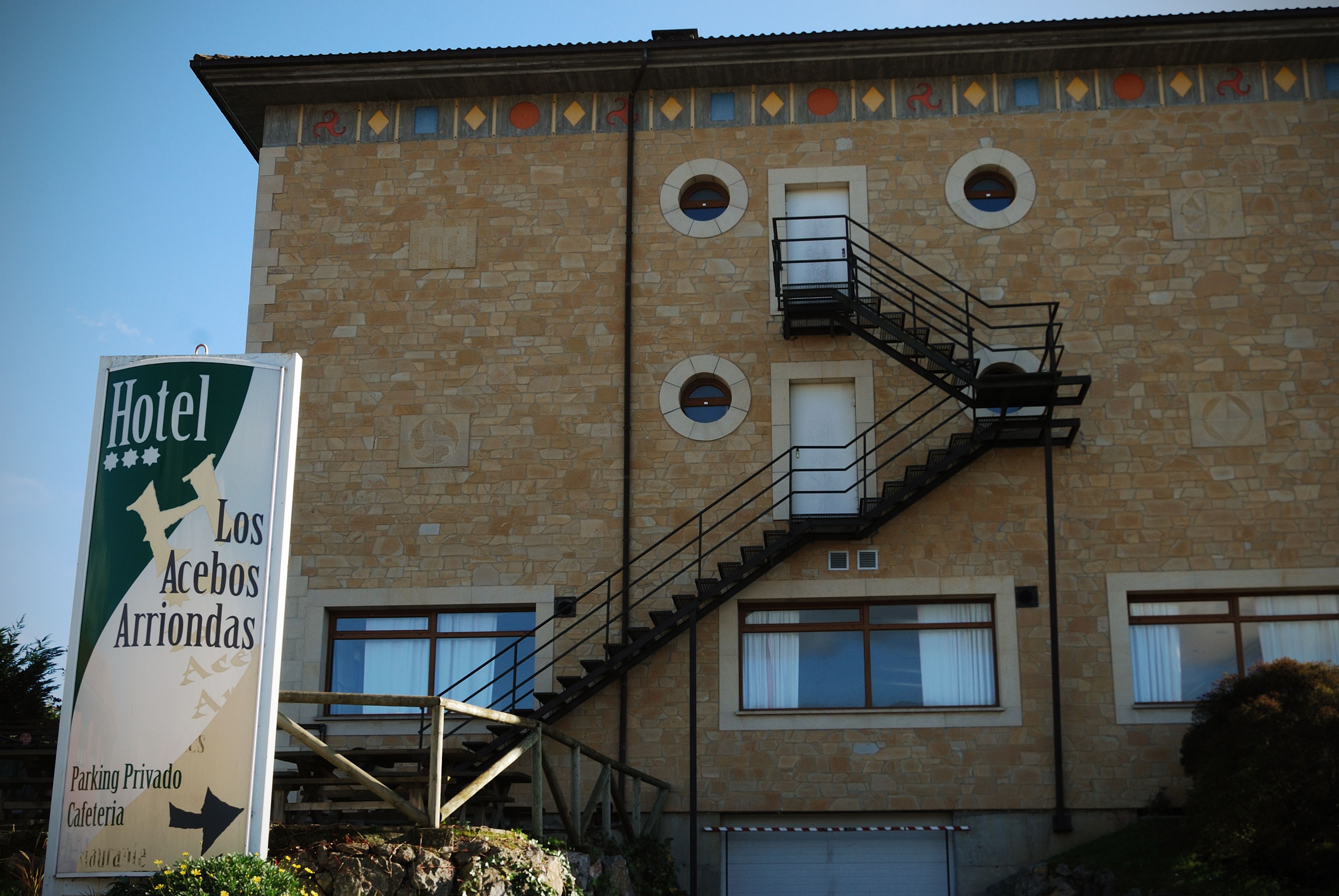 A hotel with a stone facade, a sign indicating private parking and a cafe, and a staircase leading to the entrance.