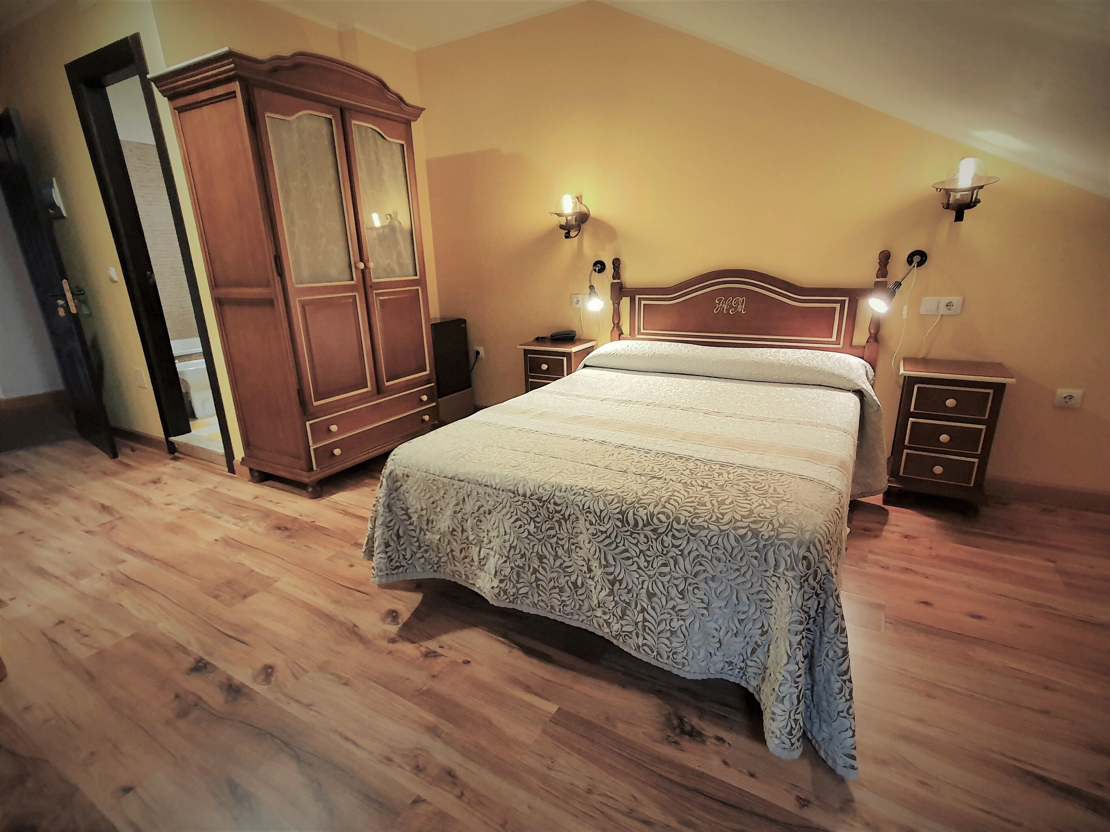 Een slaapkamer met een groot bed, een houten garderobe en bedlampjes.