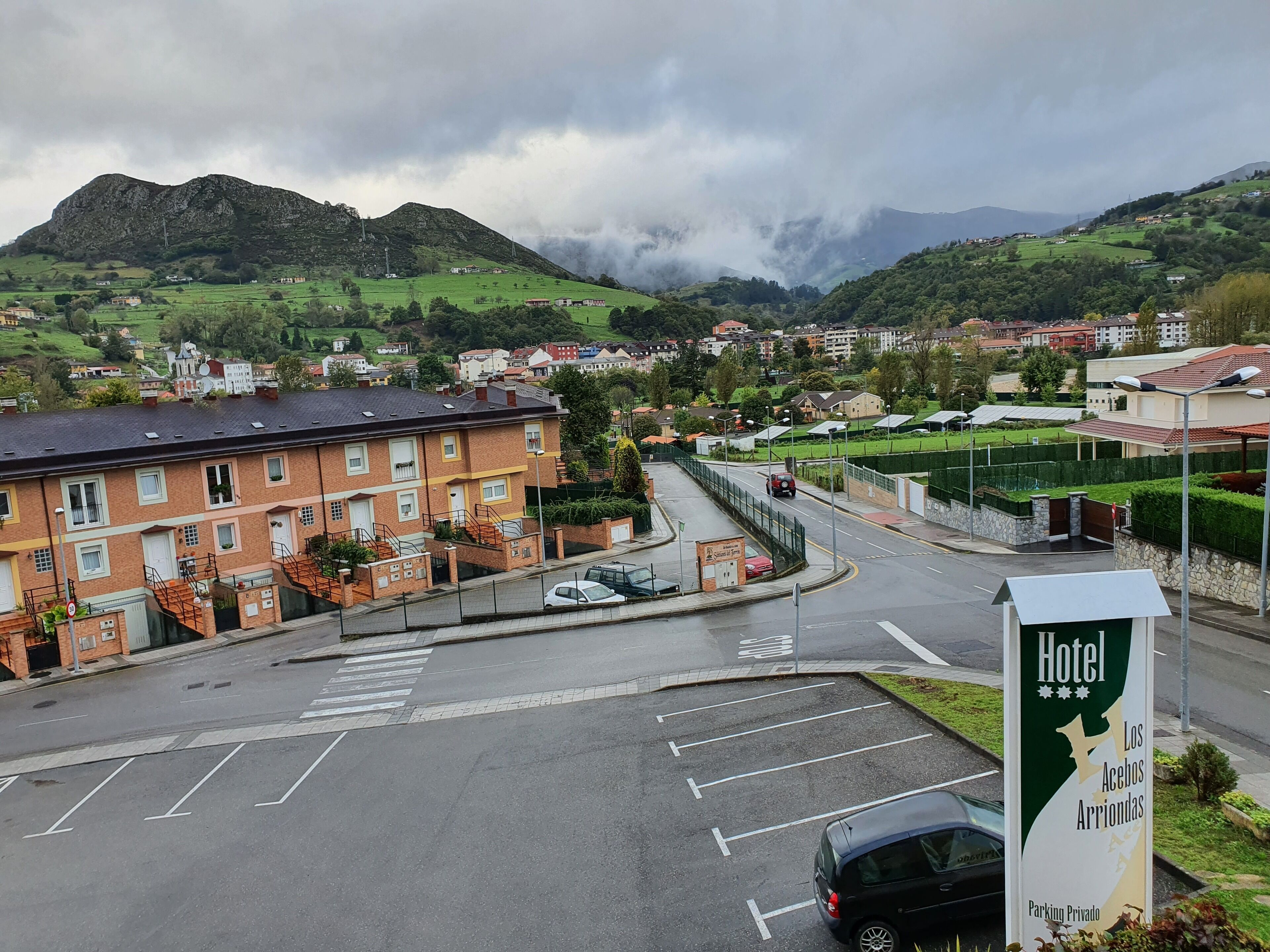 Un hotel con un cartel que indica estacionamiento privado, una carretera con un coche y un paisaje montañoso al fondo.