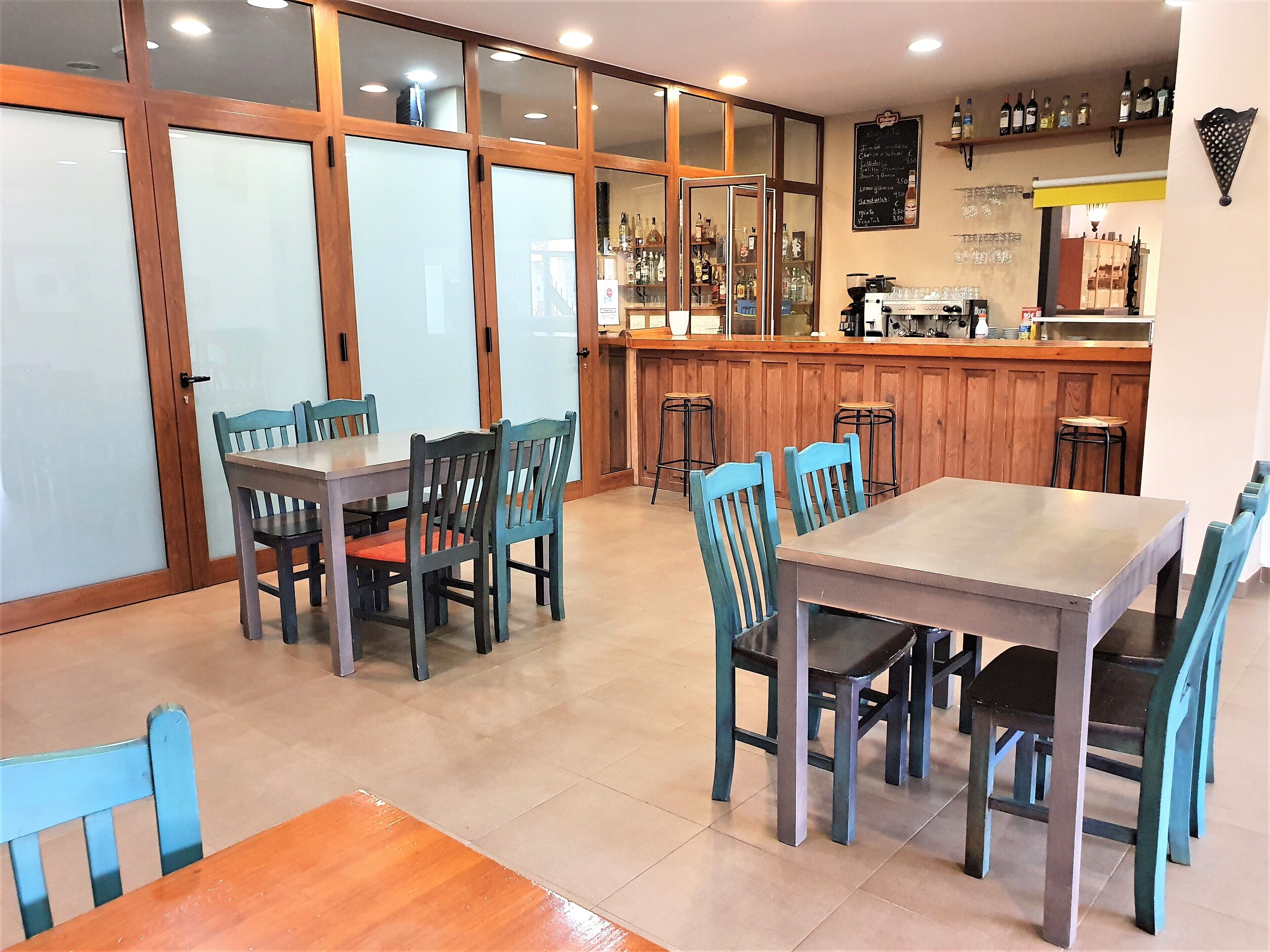 Um restaurante com mesas e cadeiras de madeira, um espaço de bar com banquetas e um quadro de menu na parede.