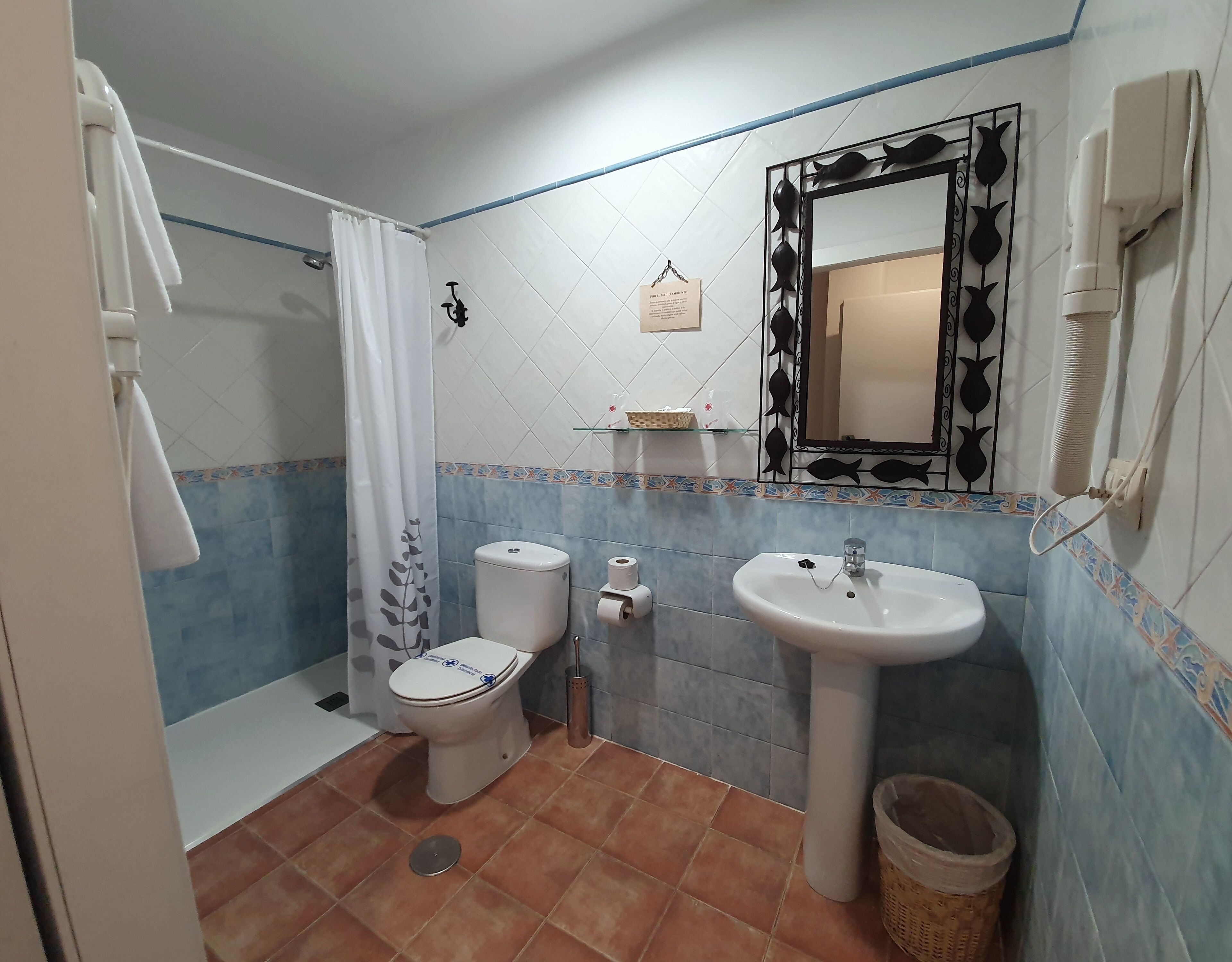 Un baño con inodoro, lavamanos, ducha y un espejo con diseños decorativos de peces.