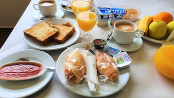 Una mesa de desayuno con tostadas, jugo de naranja, cereal, café y frutas.