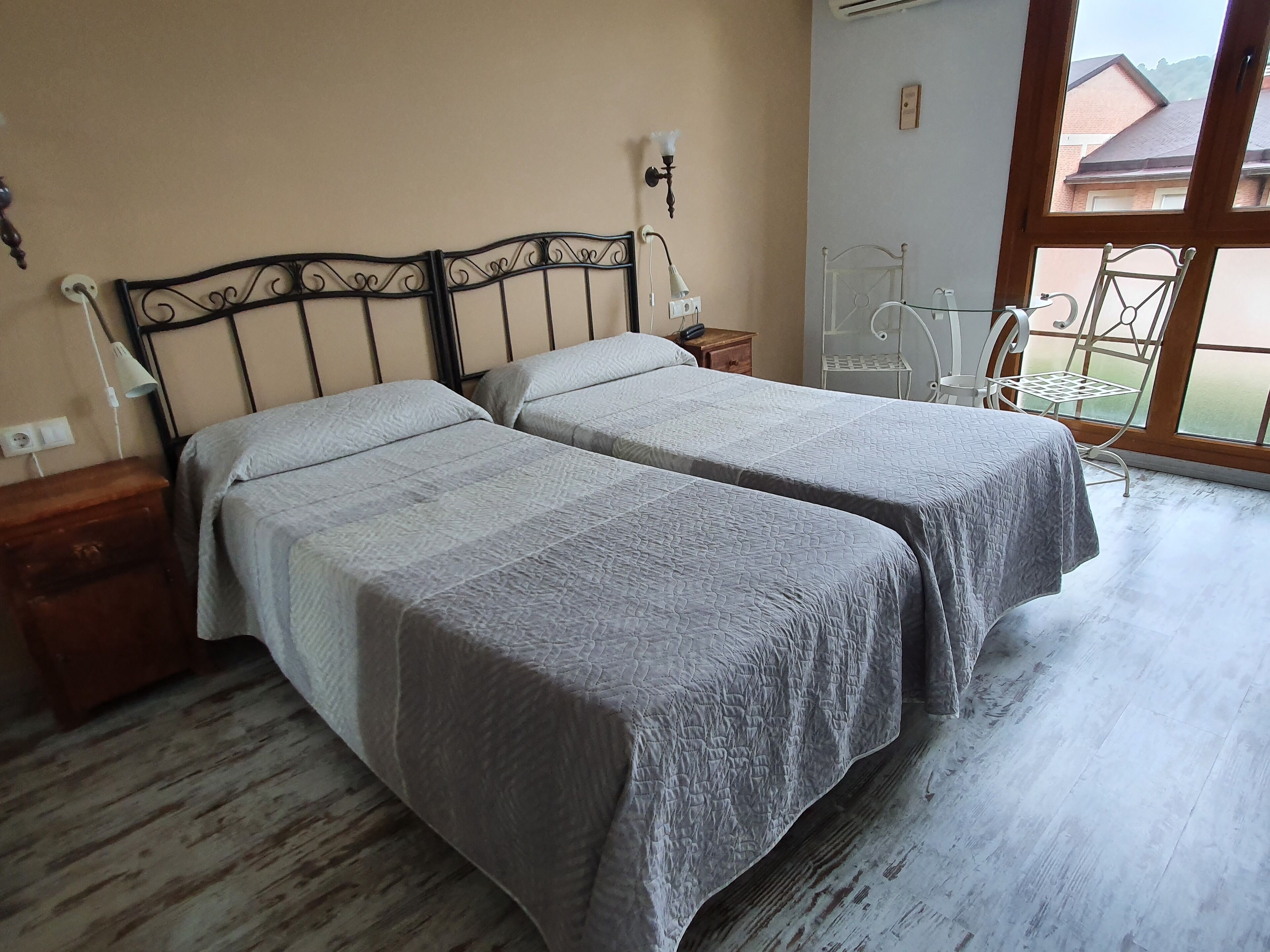 Une chambre avec deux lits, une table de chevet, une lampe et une fenêtre donnant sur des immeubles.