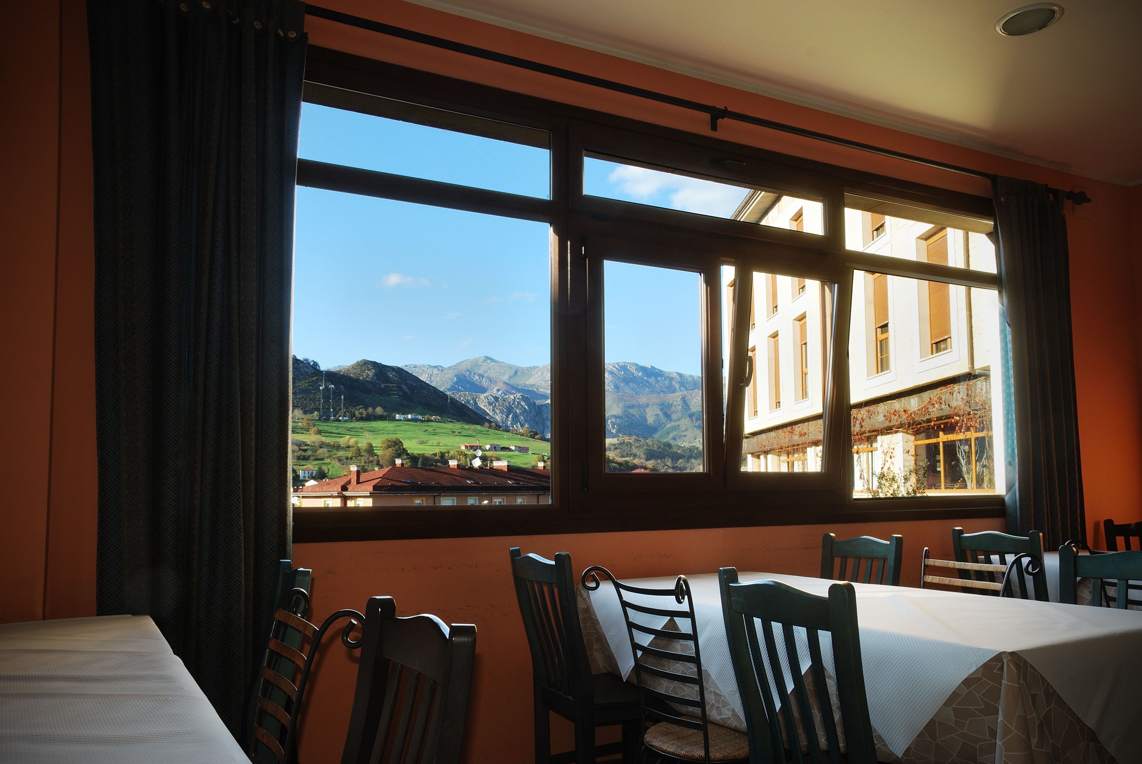 A dining area with a table and chairs, large windows with a mountain view, and a building with balconies.