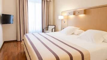 Habitación de hotel con una cama, una silla, un televisor montado en la pared y una ventana con cortinas.