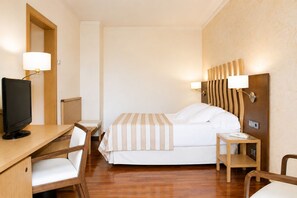 A hotel room with a bed, a desk with a computer, a chair, and a bedside table with a lamp. - Duran Hotel & Restaurant (Figueres)