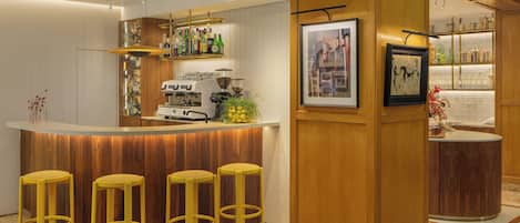 Zona de bar con taburetes, una máquina de café y estantes con botellas.