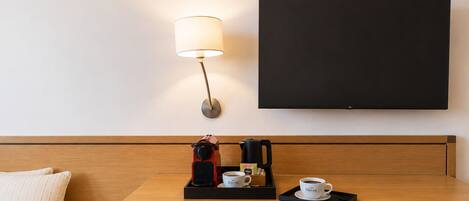 A hotel room with a wooden headboard, a table with a coffee maker, a cup, and a tray.