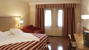 A hotel room with two beds, a desk with a television, a chair, and a large window with curtains. - Duran Hotel & Restaurant (Figueres)