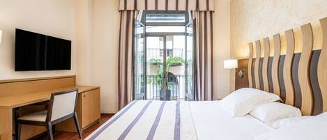 A hotel room with a bed, a desk, a television, and a view of the outdoors.