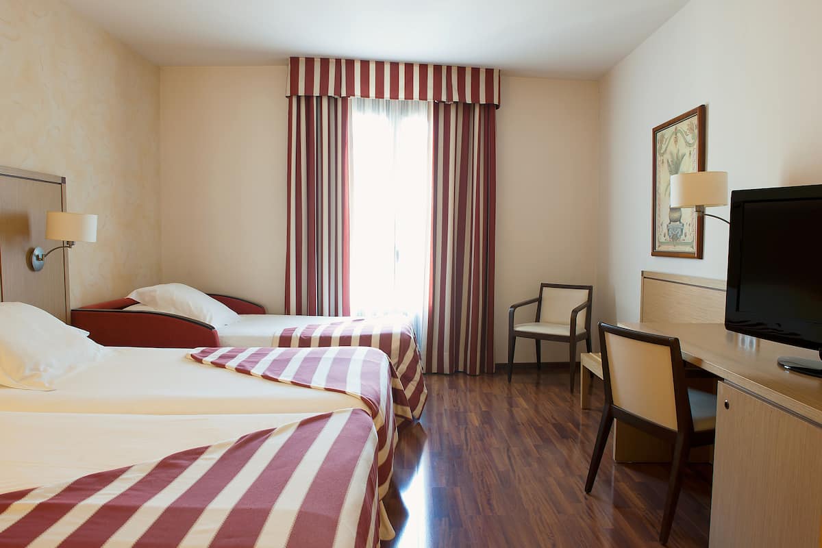 A hotel room with two beds, a desk, a chair, a television, and a window with curtains.