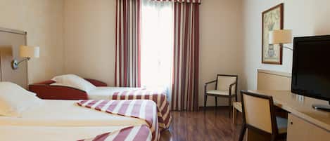 Habitación de hotel con dos camas, un escritorio, una silla, un televisor y una ventana con cortinas.