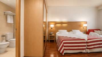 A hotel room with a wooden floor, a bed with red and white striped bedding, a nightstand with a lamp, and a bathroom with a toilet and sink.