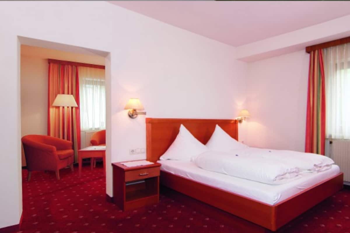 Ein Hotelzimmer mit einem Einzelbett, einem Schreibtisch, einem Stuhl und einem Nachttisch.