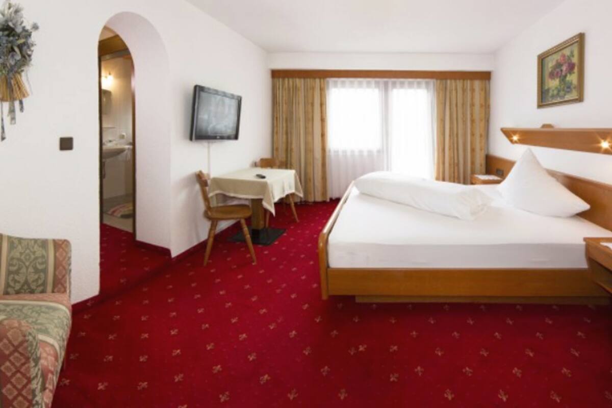 Ein Hotelzimmer mit einem großen Bett, einem Schreibtisch mit Stuhl, einem Fernseher und einem Fenster mit Vorhängen.