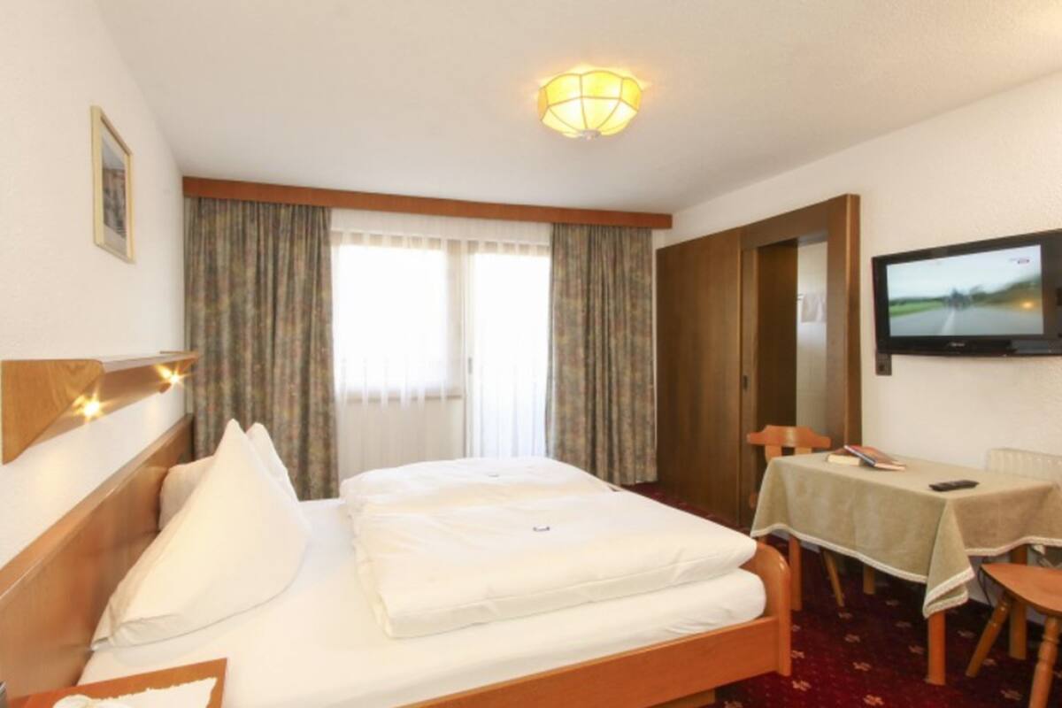 Ein Hotelzimmer mit Bett, Schreibtisch, Fernseher und Vorhängen.