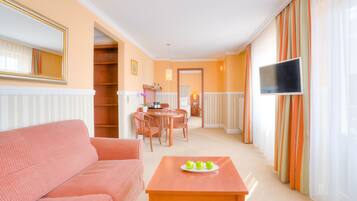 A living room with a sofa, a table with apples, a TV, and a dining area with chairs and a table.