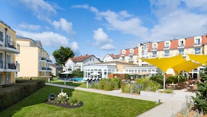 A courtyard with a swimming pool, outdoor seating, and a variety of buildings with balconies. - Hotel zur Post – ein Rovell Hotel (Heringsdorf)