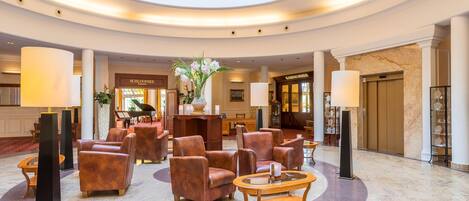 A spacious lobby with leather armchairs, a central table, and a piano.