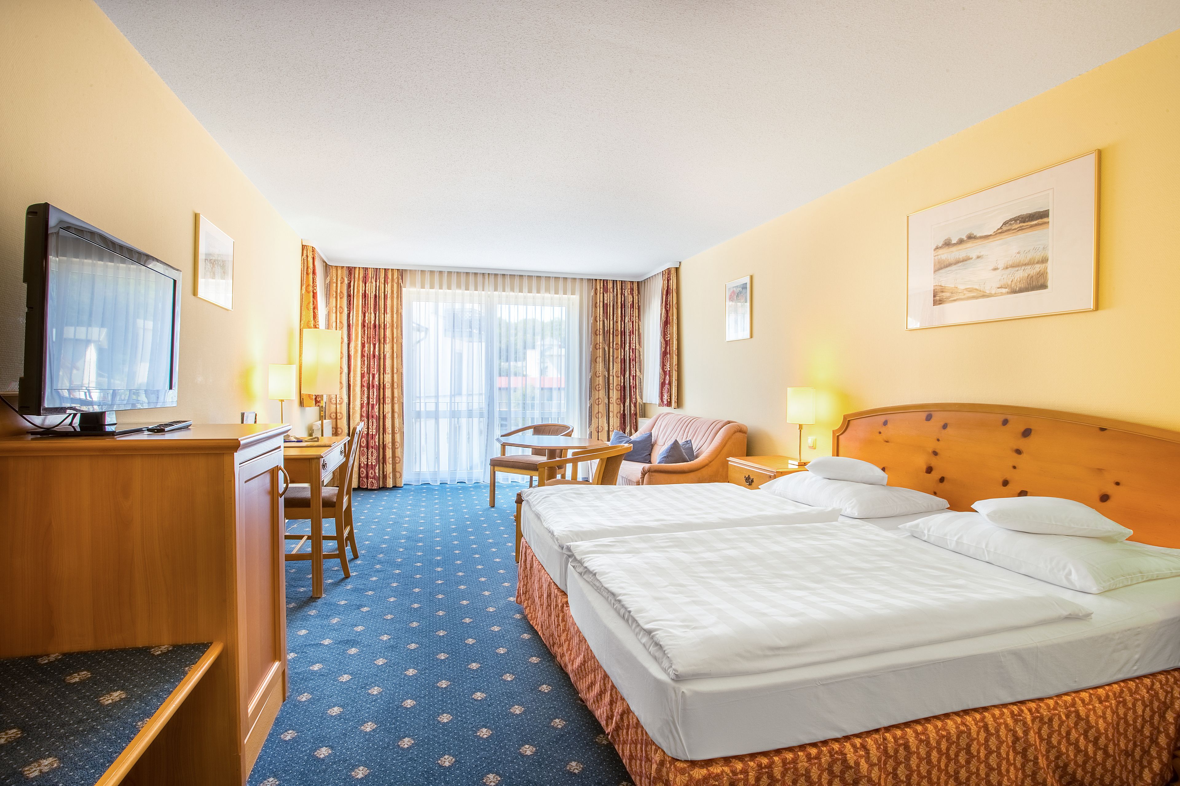 Une chambre d’hôtel avec un grand lit, un bureau avec un ordinateur, une chaise, une télévision et une fenêtre avec des rideaux.