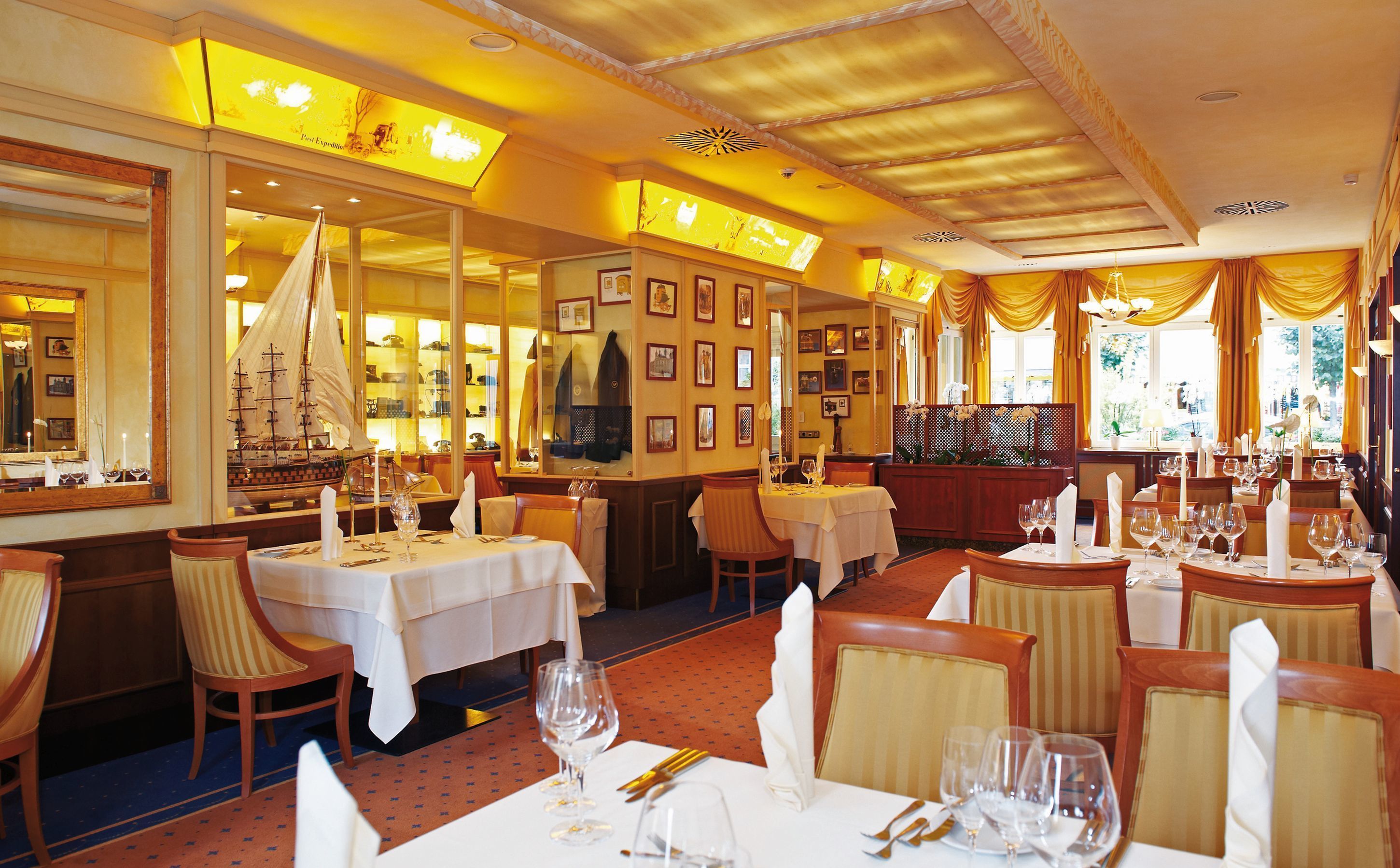 A restaurant with multiple tables set for dining, featuring a nautical theme with a ship model and framed pictures on the walls.