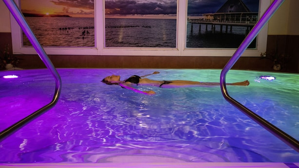 A person lying in a pool with a sunset view through a window. - Hotel zur Post – ein Rovell Hotel (Heringsdorf)