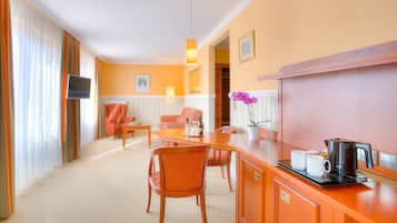 A hotel room with a dining area, a TV, a coffee maker, and a potted orchid.