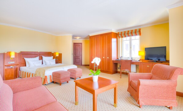 Habitación de hotel con cama, escritorio con computadora, televisor y zona de estar con sillas y mesa.