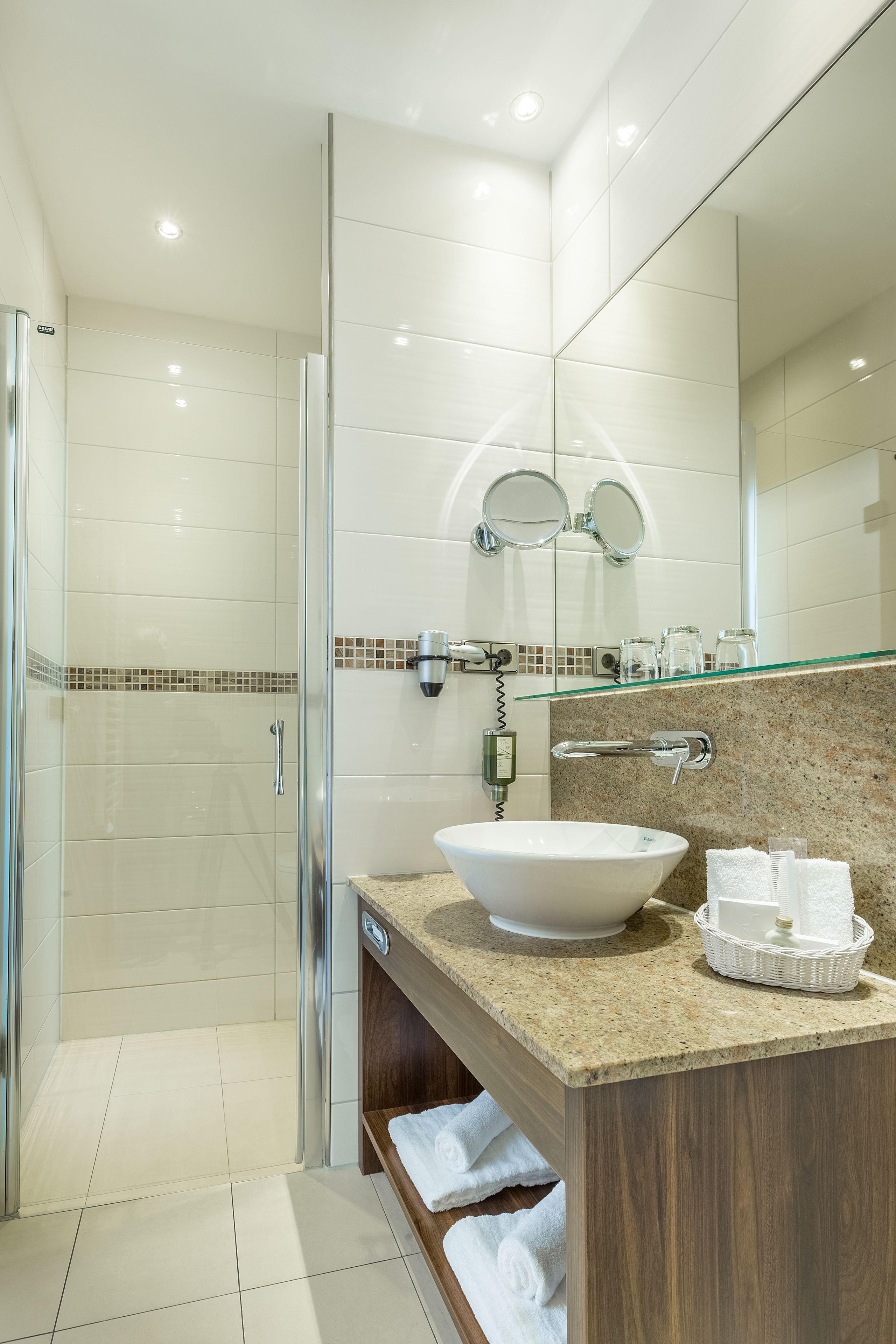 A modern bathroom with a glass shower enclosure, a large white sink, and a wooden vanity.