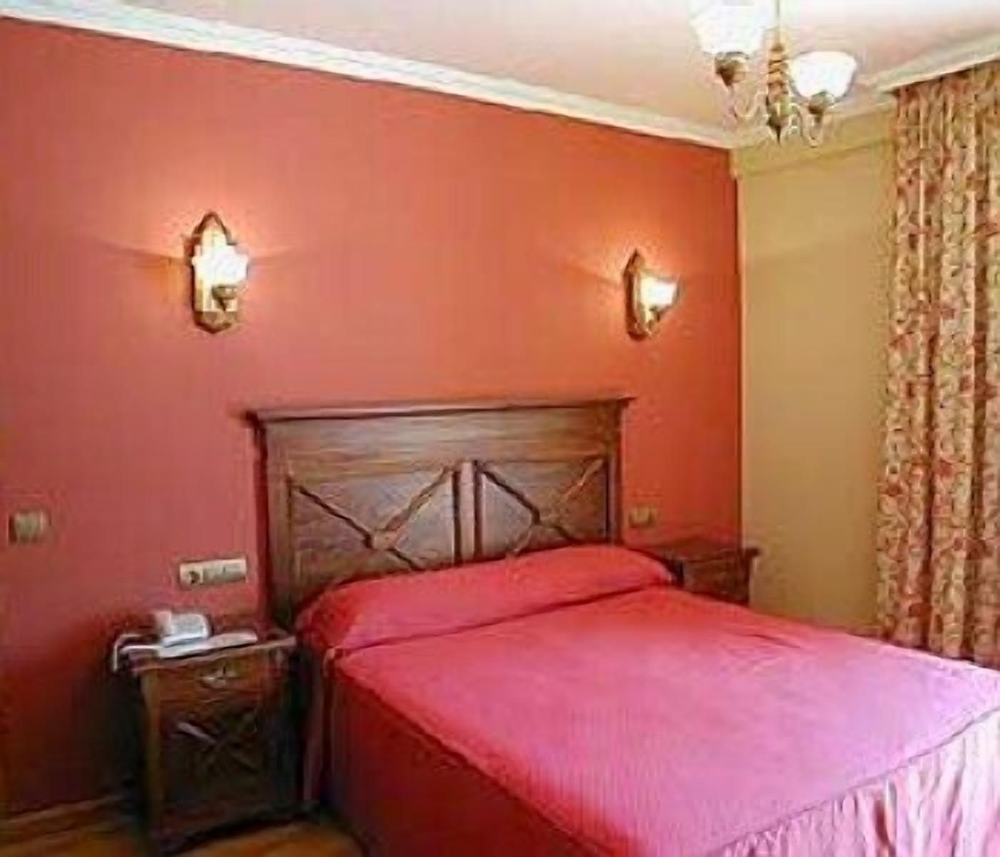 Un dormitorio con cabecera de madera, colcha roja, dos mesitas de noche y un buró.