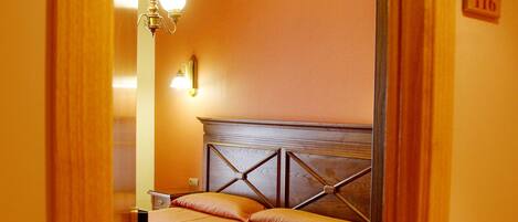 Una habitación de hotel con cabecera de madera, dos camas, una silla de madera, un escritorio y una mesita de noche.