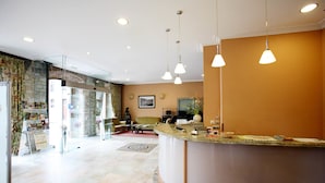 A reception area with a curved counter, a sofa, a coffee table, and a desk with a computer. There are hanging pendant lights and a framed picture on the wall. - Hotel Imperion (Parres)