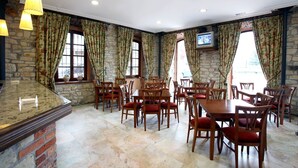 A restaurant with stone walls, wooden tables and chairs, and a TV mounted on the wall. - Hotel Imperion (Parres)