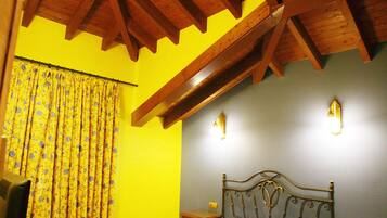 A bedroom with a wooden ceiling, a bed, a nightstand, a lamp, and a curtain.