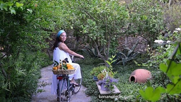 Una persona montando en bicicleta en un jardín exuberante, llevando una canasta de frutas y verduras.