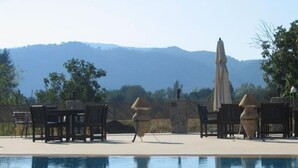 A pool area with lounge chairs and a table, surrounded by a fence, with a mountain view in the background. - Misafir Evi Hotel (Fethiye)