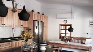 A modern kitchen with wooden cabinets, a stainless steel refrigerator, a black countertop, and a dining area with a wooden table and bench. - Misafir Evi Hotel (Fethiye)