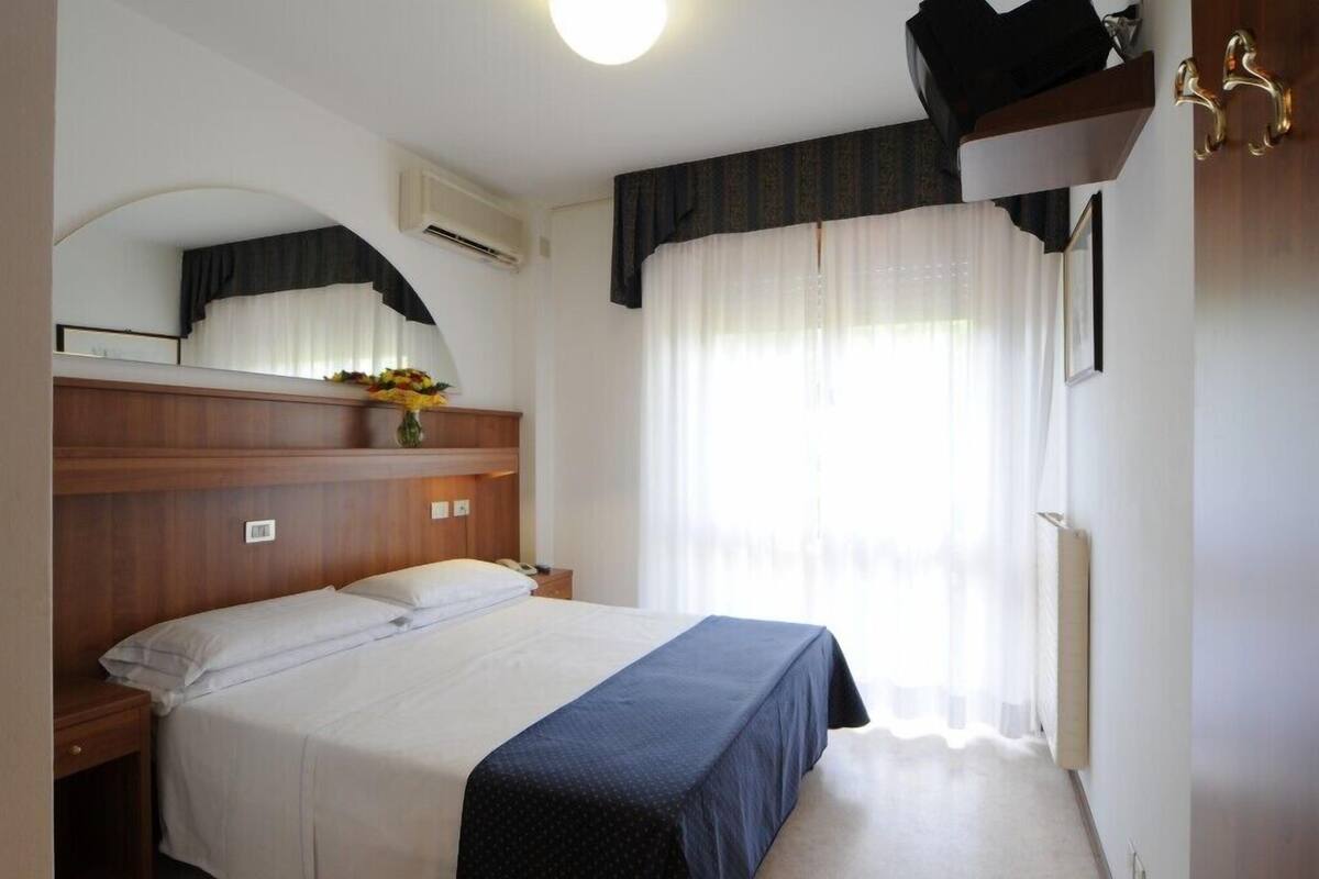 Hotelkamer met een bed, nachtkastje, spiegel, raam met gordijnen en een wandradiator.