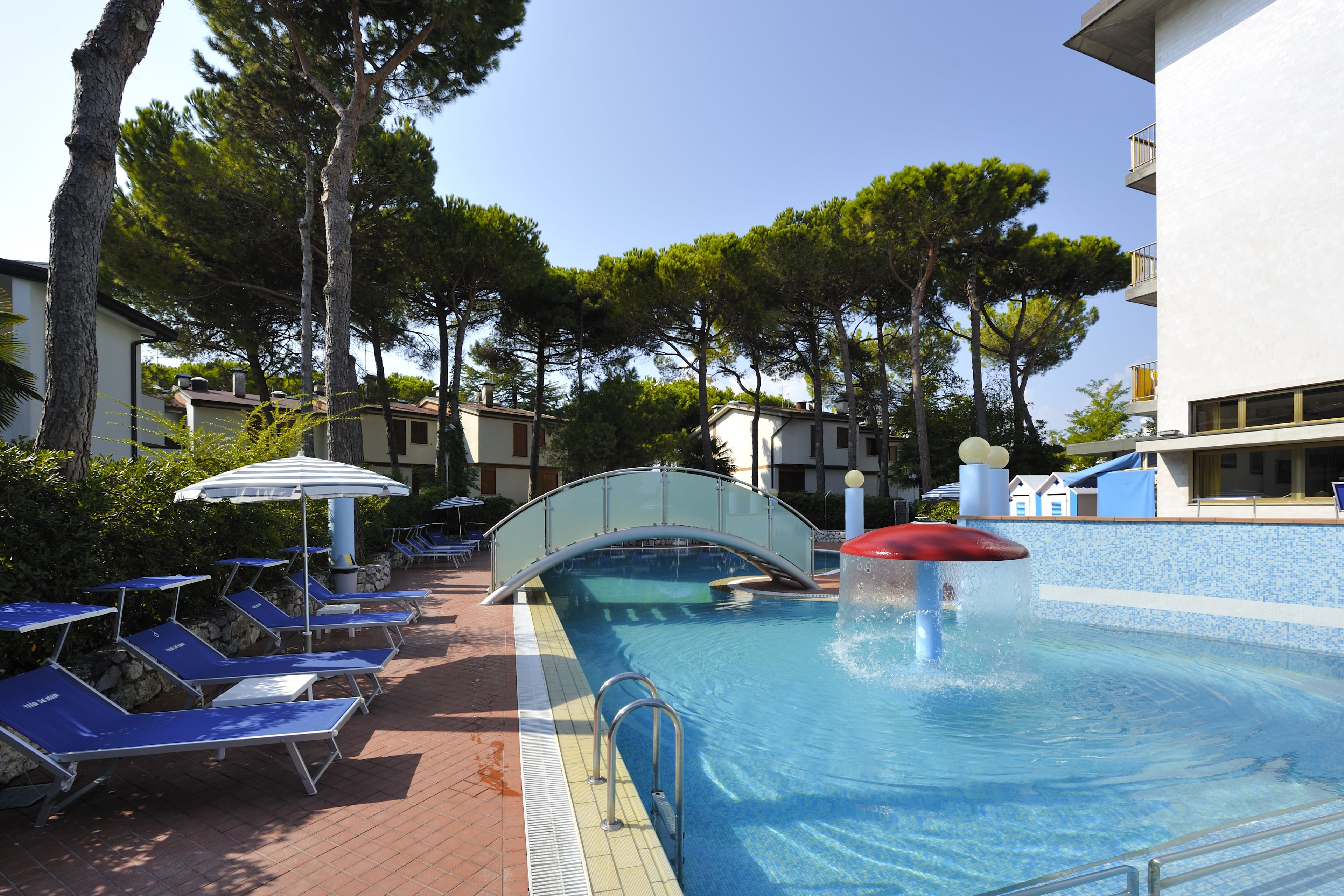Une piscine avec des chaises longues, un pont et des arbres.