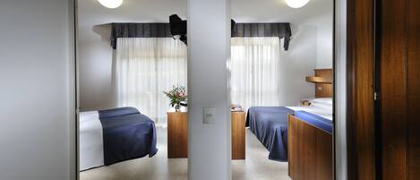 A hotel room with two beds, a wooden dresser, a nightstand, and a small table with a vase of flowers.