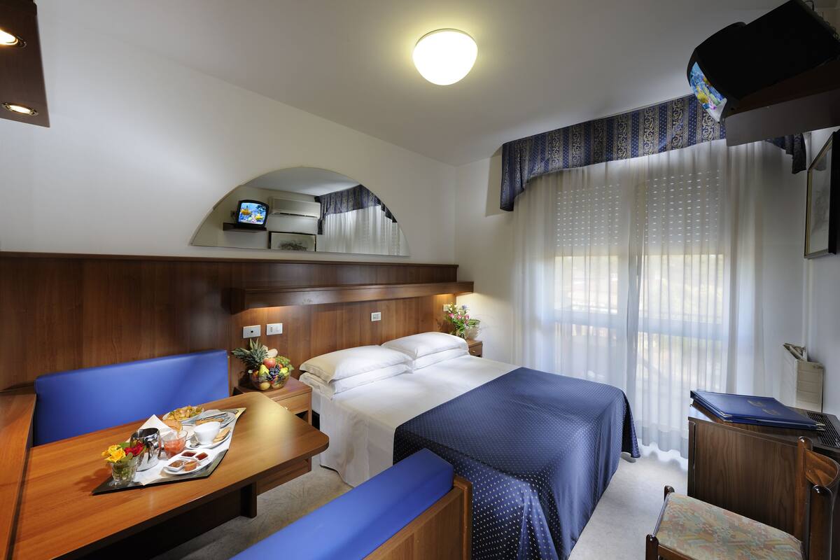 Een hotelkamer met een bed, een bureau, een stoel, een televisie en een raam met gordijnen.