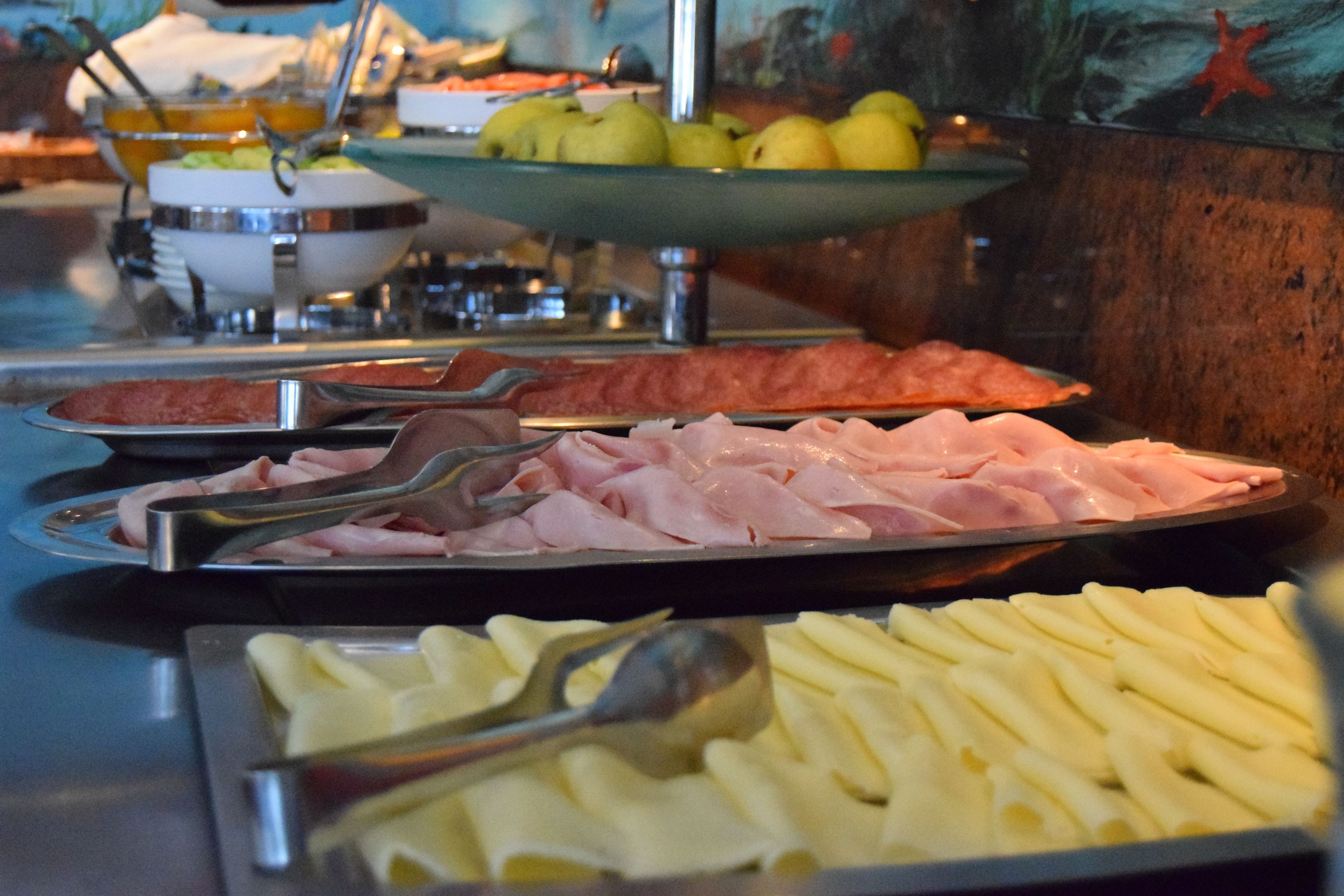 Buffet com diversas opções de comida, incluindo carnes fatiadas, queijos e frutas.